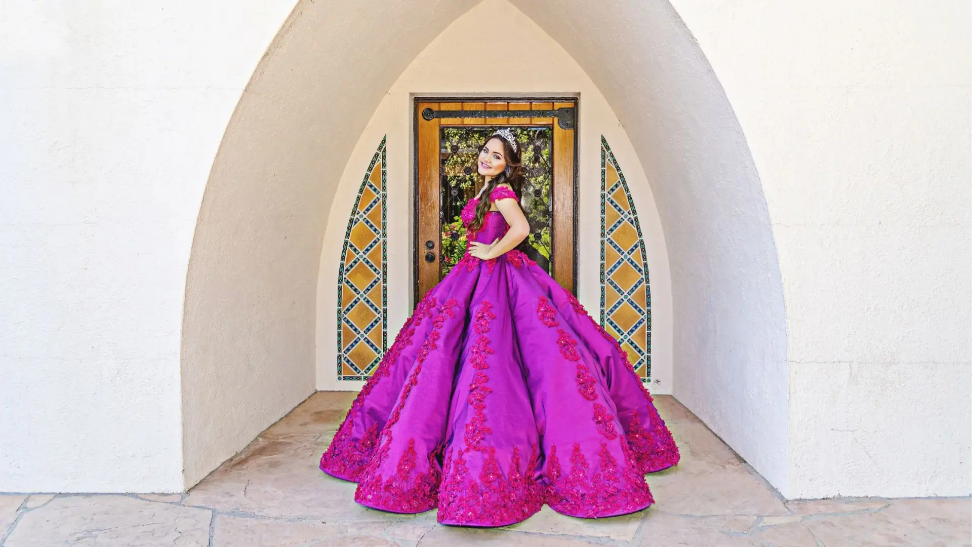 Magenta ballgown with tiara framed by an arch doorway