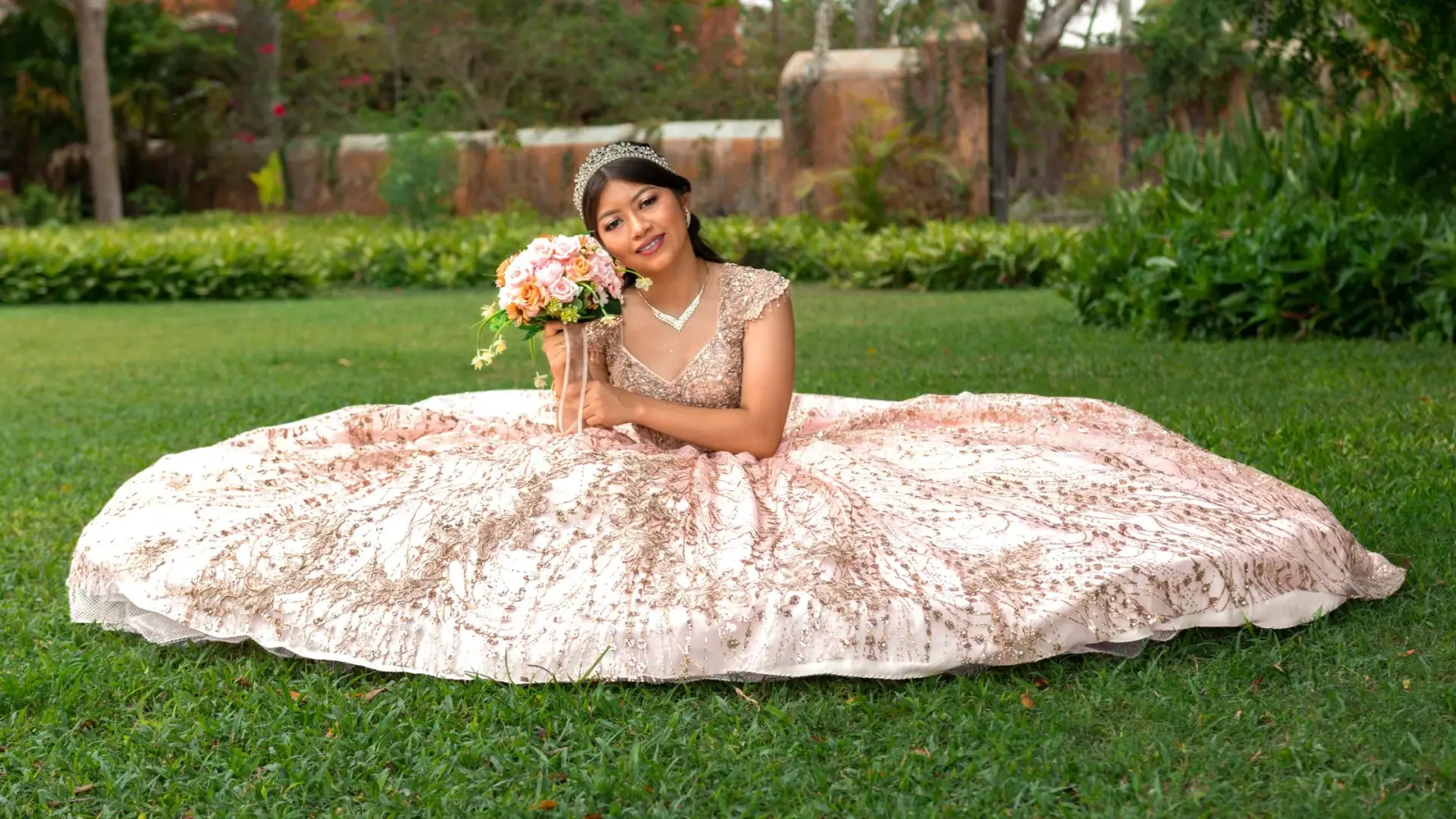 Rose-gold sparkle ballgown with tiara, seated in garden