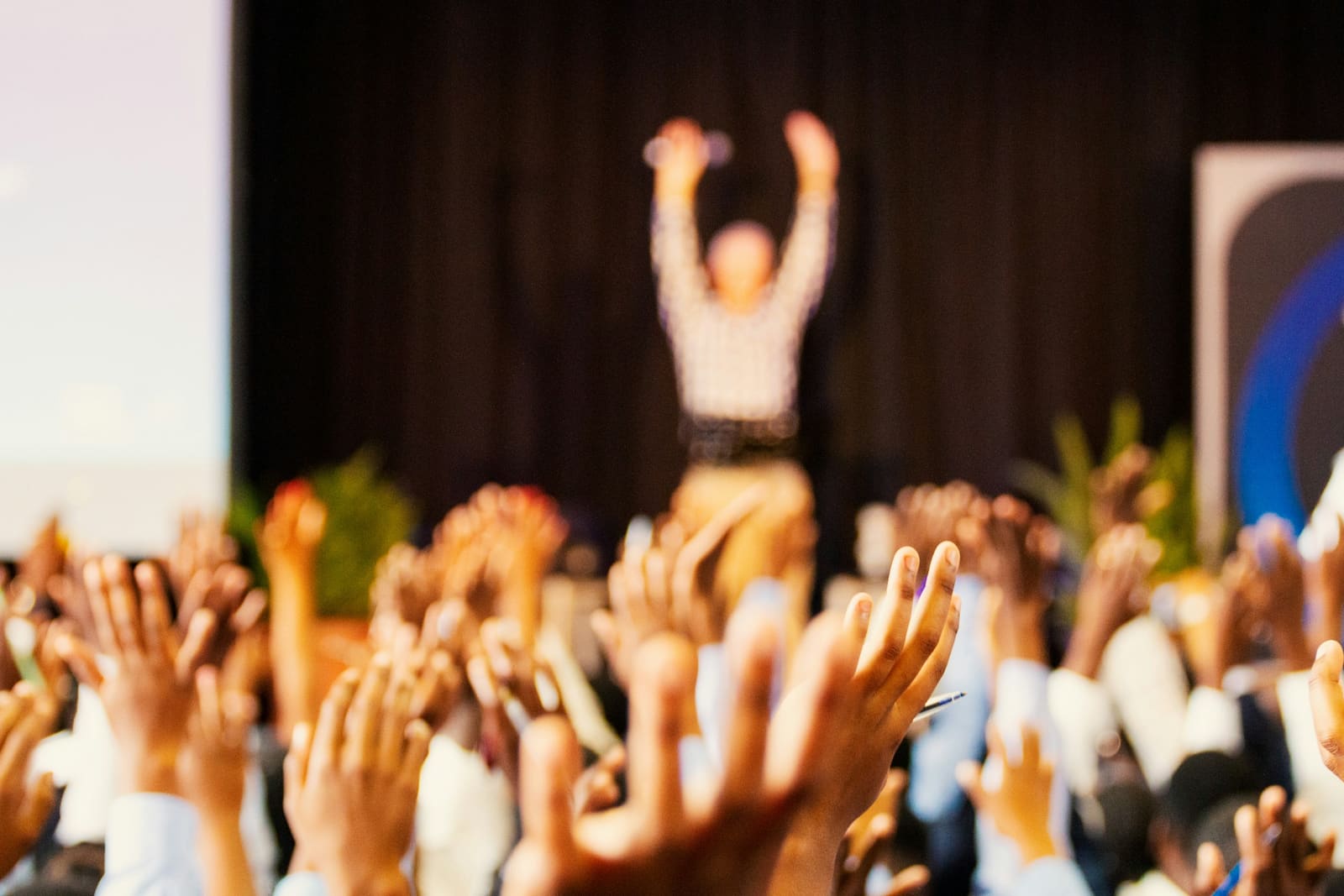 Speaker on stage with audience hands raised under bokeh lighting