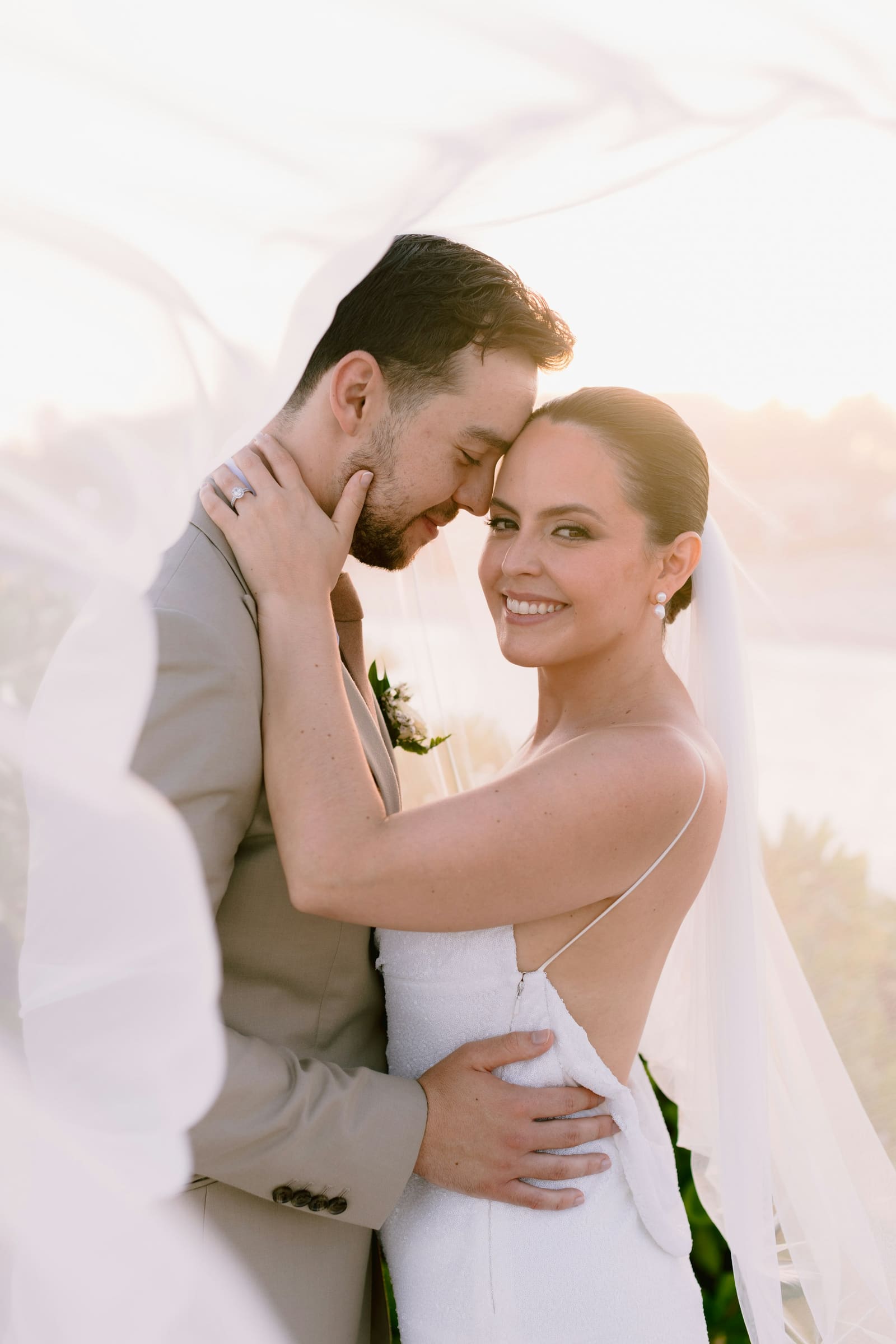 A bride and groom embracing under a luminous golden veil at sunset