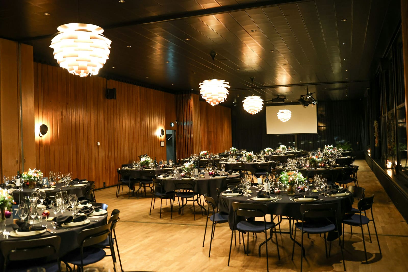 Premium corporate ballroom set for dinner: round tables, statement chandeliers, ambient evening lighting