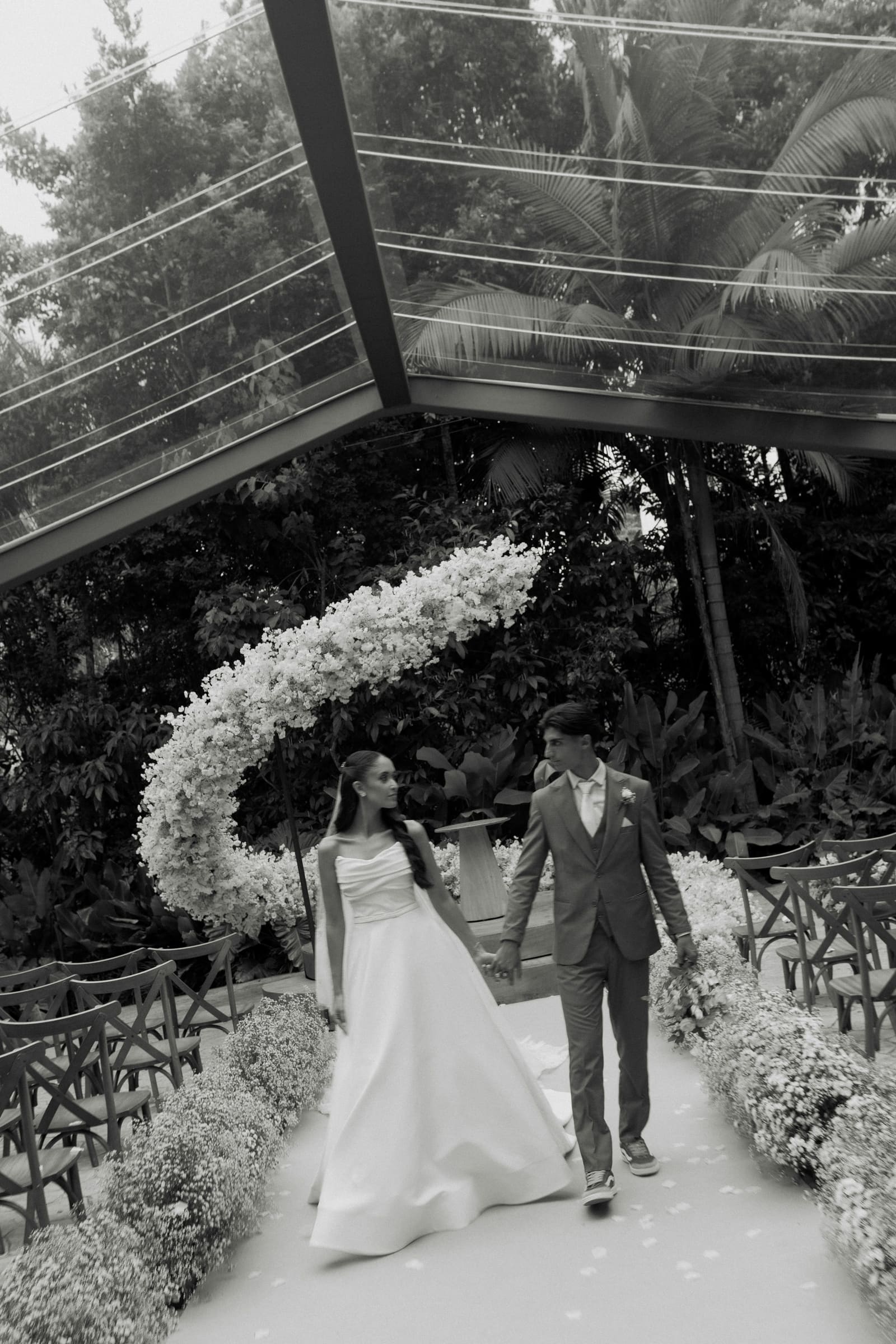 Bride and groom walking down the aisle past a sculptural white floral arch