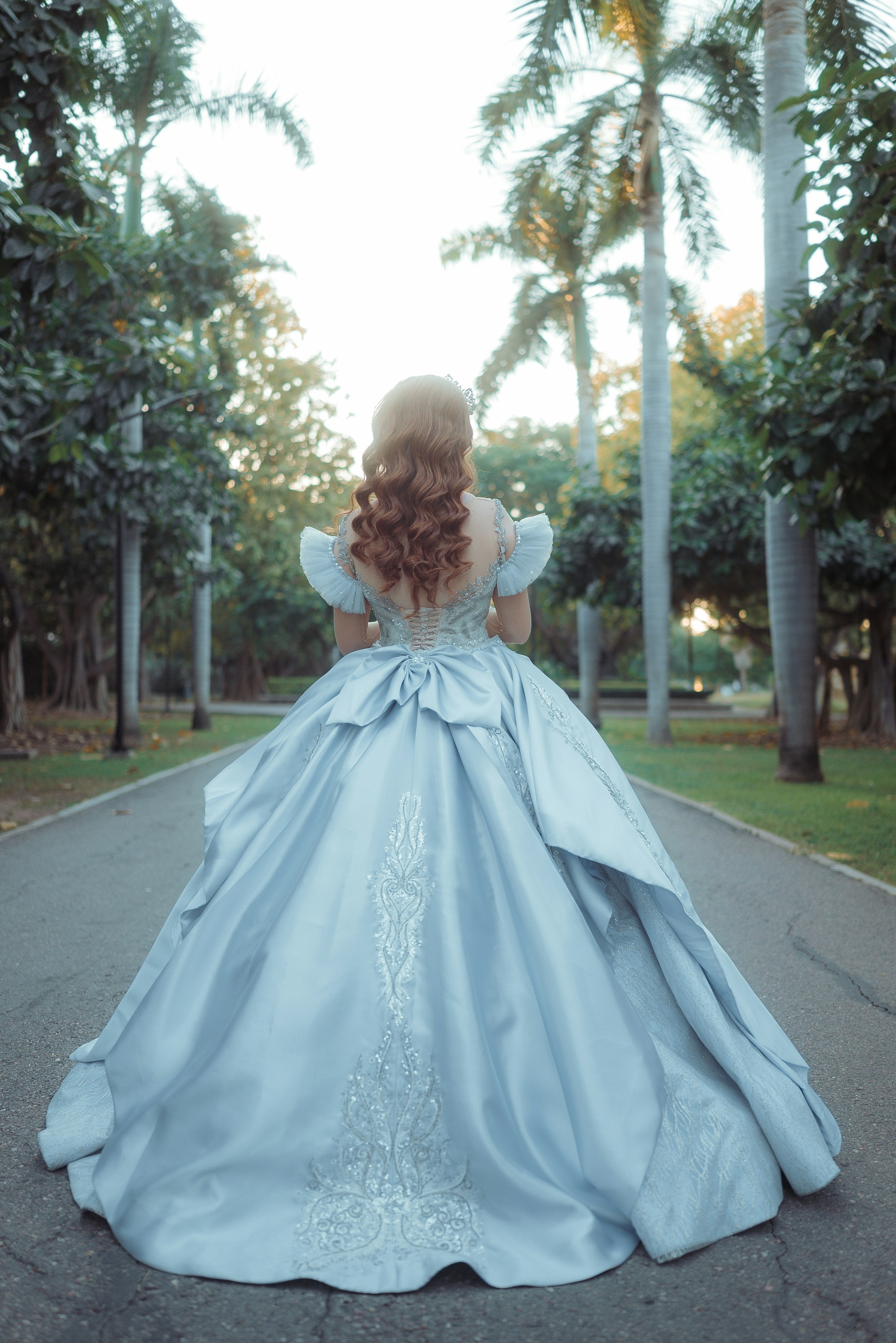 Quinceañera in elegant blue ballgown walking through a park (Unsplash · @quincesperfectos)