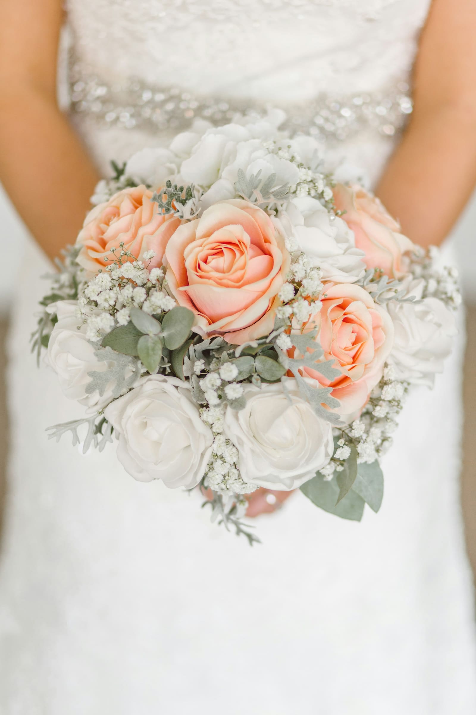 Bride holding a close-up bouquet of white and blush pink roses with eucalyptus